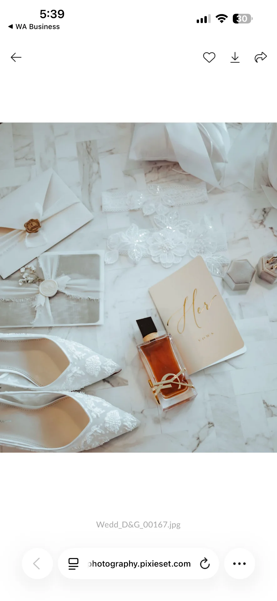 Zapatos, perfume y papelería de boda dispuestos sobre tela blanca